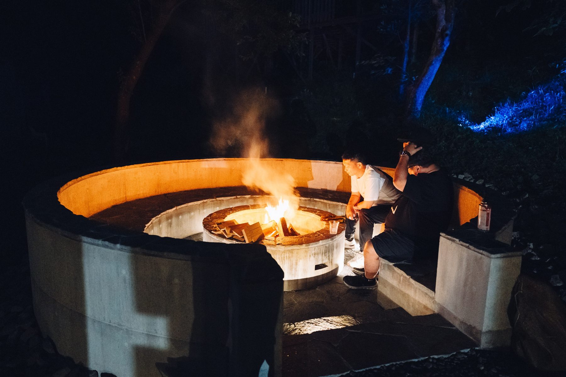 夜、円形の焚火場の中央で火が燃え、煙が立ちのぼっている