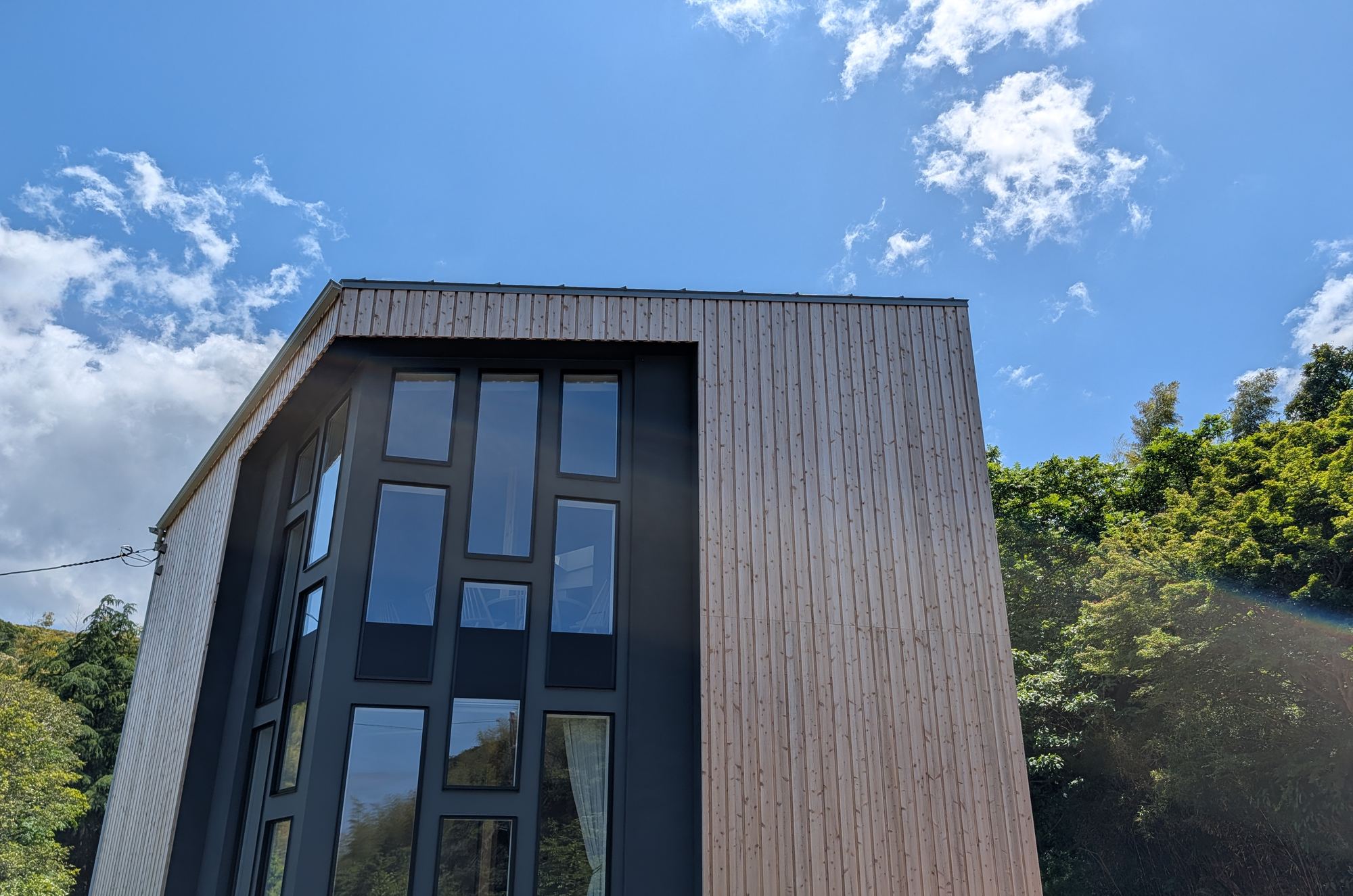 青空の下、木を張った建物。大きなガラス面が森に向いている